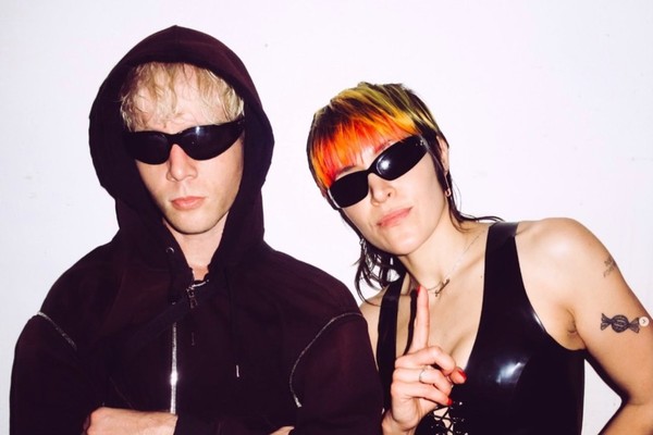 Duo Sextile are both in dark sunglasses, faced toward the camera, with a neutral background