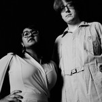 Black and white photo of duo Sweeping Promises, standing posed with their gaze downward toward the camera.