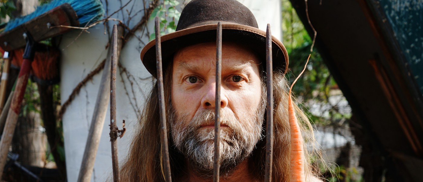 Photo taken outdoor of Thor Harris holding a pitchfork in one hand with a carrot in the other.
