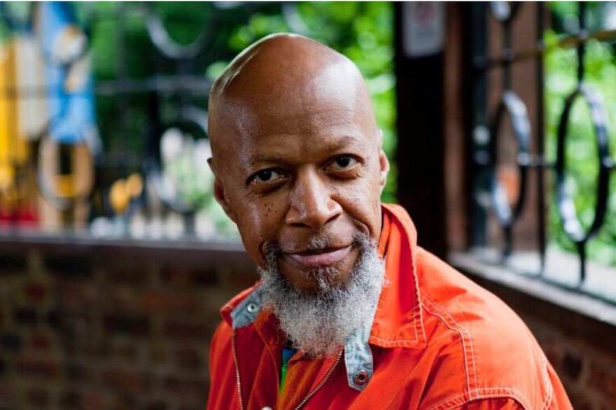 Photo of solo artist Laraaji, posed facing the camera wearing an orange coat.