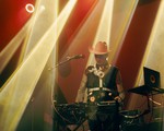 Christopher Fleeger of Cooling Prongs captured onstage, performing on a keyboard, bathed in yellow and red lighting, wearing a bright cowboy hat and boots.