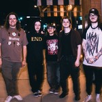 A colour photo of five-piece band Atrology Girl standing on a sidewalk outside of a brick building. 