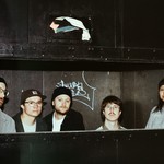 A colour photo of five-piece group Bad Bodies standing inside a cardboard compressor. They are seen from the neck and shoulders up.