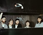 A colour photo of five-piece group Bad Bodies standing inside a cardboard compressor. They are seen from the neck and shoulders up.
