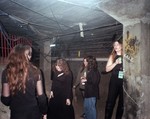 A candid colour photo shows five-piece group Babe Corner standing under a dingey concrete structure. Several members are holding cans of beer. 