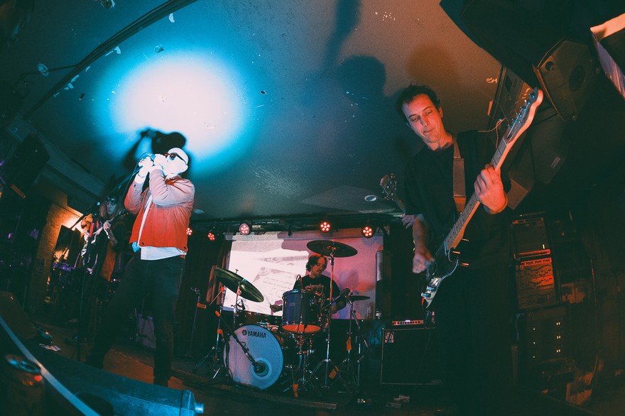 A colour photo taken from below shows four-piece BRIDGELAND playing on stage with blue and red lights shining on the members. 