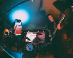 A colour photo taken from below shows four-piece BRIDGELAND playing on stage with blue and red lights shining on the members. 
