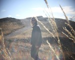A grainy colour photo shows aritst Brock Geiger walking in a park with long strands of wheat in the foreground.