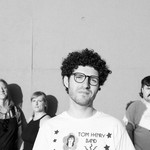 A black and white photo shows four-piece band Buddie standing in front of a white concrete wall. 