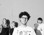 A black and white photo shows four-piece band Buddie standing in front of a white concrete wall. 