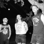A black and white photo shows three-piece group Cell Press standing outside with a large tree to the far right. 