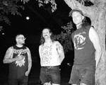 A black and white photo shows three-piece group Cell Press standing outside with a large tree to the far right. 