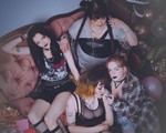 Four-piece group dead ex girlfriends are shown in a messy living room sitting on the couch and on the floor looking distraught, with a few members smoking cigarettes.