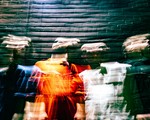 A vibrant long exposure photo shows four-piece band cute standing un front of a dark brick wall. Their faces and bodies are distorted due to the camera effect. 