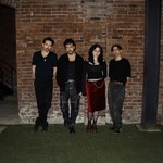 A colour photo shows four-piece group DOUR on a patch of grass standing against a brick wall at night.