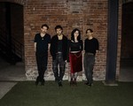 A colour photo shows four-piece group DOUR on a patch of grass standing against a brick wall at night.