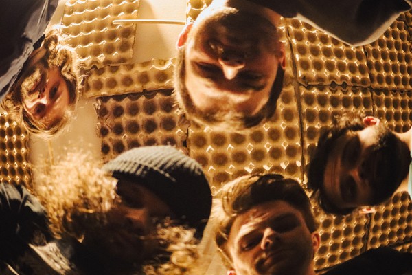 A hazy photo taken from below shows five-piece band looking down at the camera with a golden roof above that appears to be lined with egg cartons. 