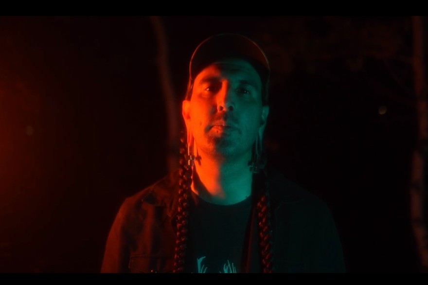 A close-up colour photo of artist ECHTHROS standing outside at night with blue and red light shining on their face. 