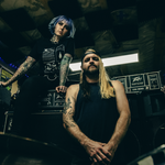 A colour photo taken from below shows the duo FRANKLIN sitting in what looks like a jam space filled with amps and guitars. 