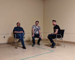 Three members of the band Fulfilment sit on black chairs in a empty beige room and look at the camera.