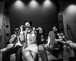 A black and white photo shows the four members of the band Ginger Beef sitting on a couch with guitars on each side. One member second from the left holds a tie in front of their face covering their nose. 