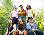A colour photo shows six-piece band Hip Hip Thursday standing outside with leafy trees behind them. Three members sit on a rock in the foreground, while three members stand behind them. 