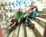 A colour photo shows four-piece group innerouter sitting outside on concrete stairs, with each member on a different step.The setting that resembles the enrtrance to an old train station, graffiti fills the concrete wall behind them.
