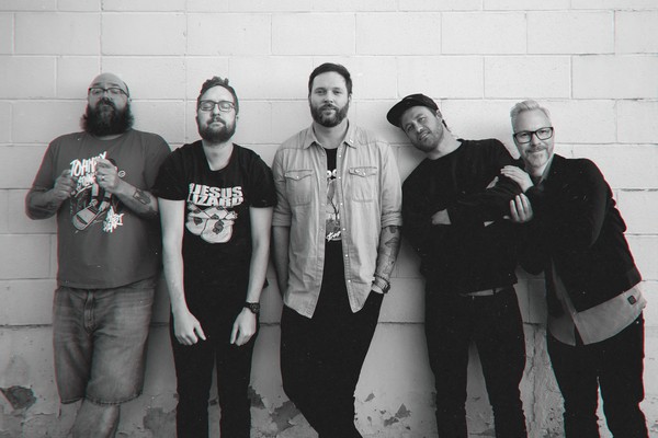 A black and white photo shows five-piece band Julius Sumner Miller standing in front of a white brick wall.