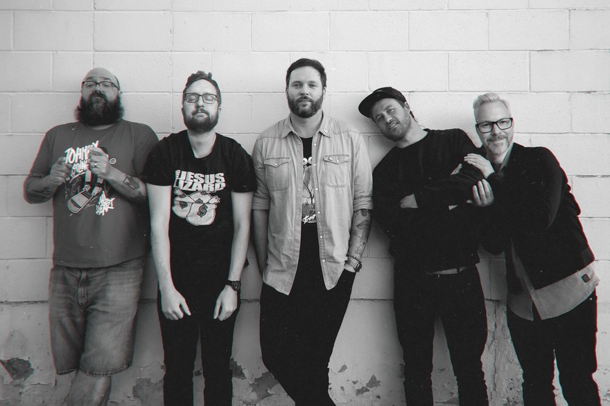 A black and white photo shows five-piece band Julius Sumner Miller standing in front of a white brick wall.