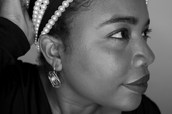 A close-up photo shows artist MAGELLA looking sideways with a long string of white pearls strung around the top of their head. 