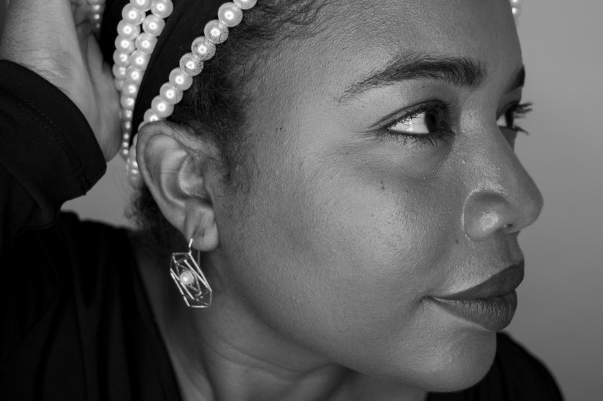 A close-up photo shows artist MAGELLA looking sideways with a long string of white pearls strung around the top of their head. 