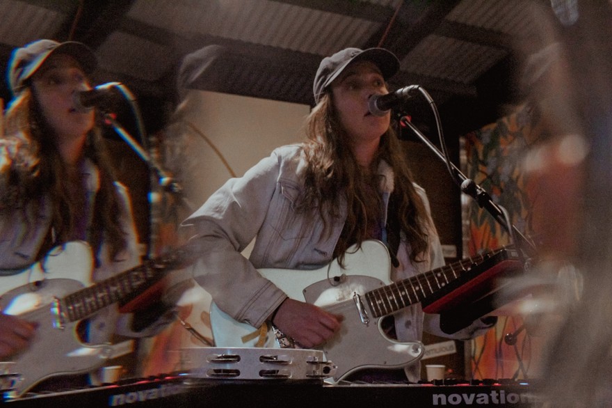 A double exposure photo shows frontperson of the project mon cher playing a white electric guitar and singing into a microphone. 