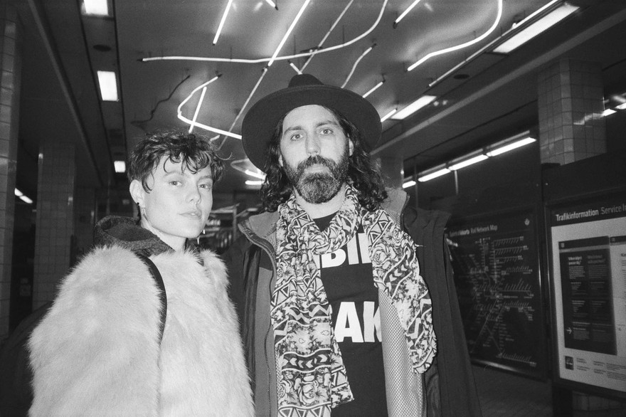 A black and white photo shows duo MOONBEAN standing in an underground train station looking at the camera. 