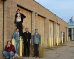 Five members of the band NON ULTRAS are seen standing in an old alleway against a brick building. One member in the middle is seen standing on top of a yellow concrete post. 