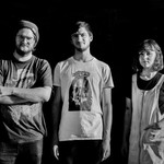 A black and white photo shows four-piece group Pike standing in a line with a dark black background behind them. 