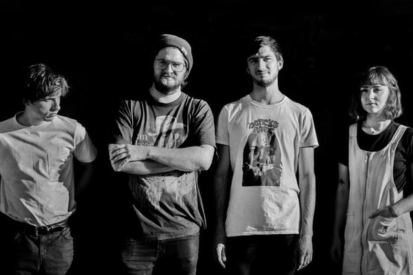 A black and white photo shows four-piece group Pike standing in a line with a dark black background behind them. 
