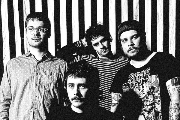 A fuzzy black and white photo shows four-piece Pnoom posing in front of a black and white striped wall. 