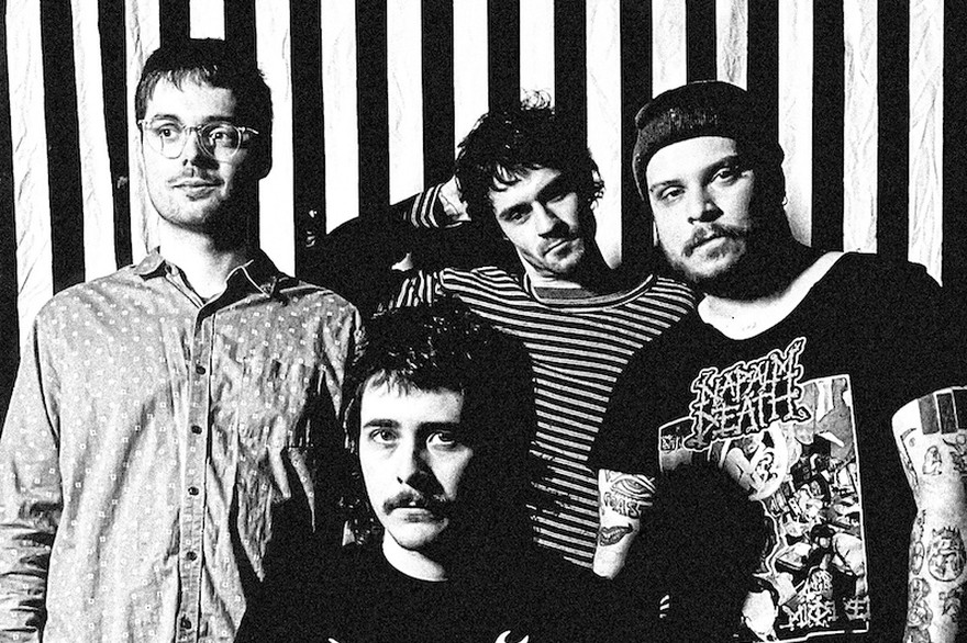 A fuzzy black and white photo shows four-piece Pnoom posing in front of a black and white striped wall. 