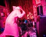A photo bathed in red light shows the duo Radioactive Vampire Teeth performing on the stage upstairs at The Palomino. The drummer is seen performing the background, and the frontperson looks to be smashing the symbals from the front. 