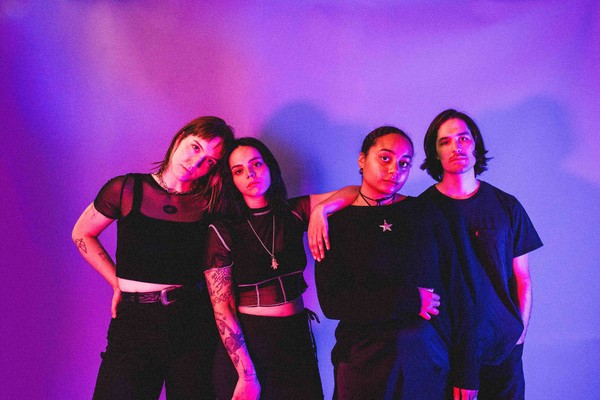 The four-piece group Roach are shown standing in a line wearing all black against a purple background. 