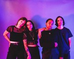 The four-piece group Roach are shown standing in a line wearing all black against a purple background. 