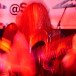 A hazy colour photo bathed in red light shows a member of the band SENTRIES playing a guitar. A long exposure effect distorts the photo.