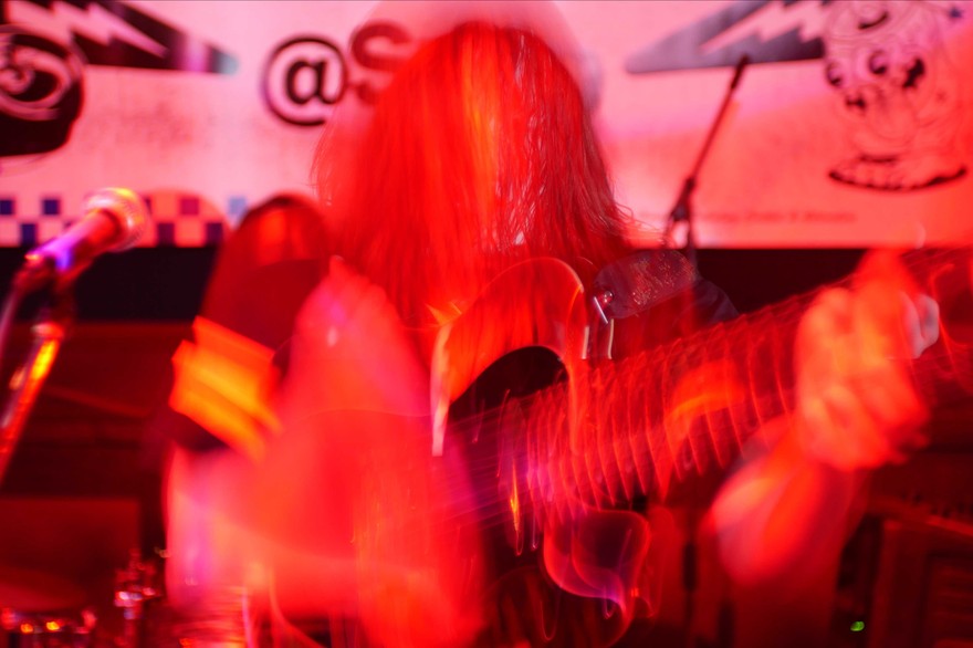 A hazy colour photo bathed in red light shows a member of the band SENTRIES playing a guitar. A long exposure effect distorts the photo.