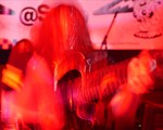 A hazy colour photo bathed in red light shows a member of the band SENTRIES playing a guitar. A long exposure effect distorts the photo.