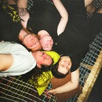A grainy colour photo shows four members of the group Sick Puppy laying in a hammock looking up with the photo being taken from above.