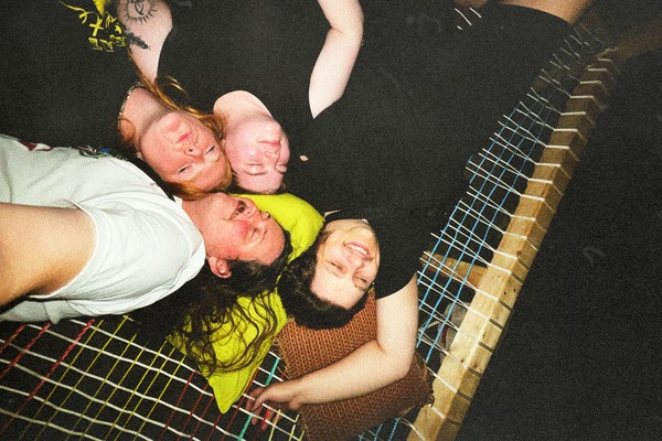 A grainy colour photo shows four members of the group Sick Puppy laying in a hammock looking up with the photo being taken from above.