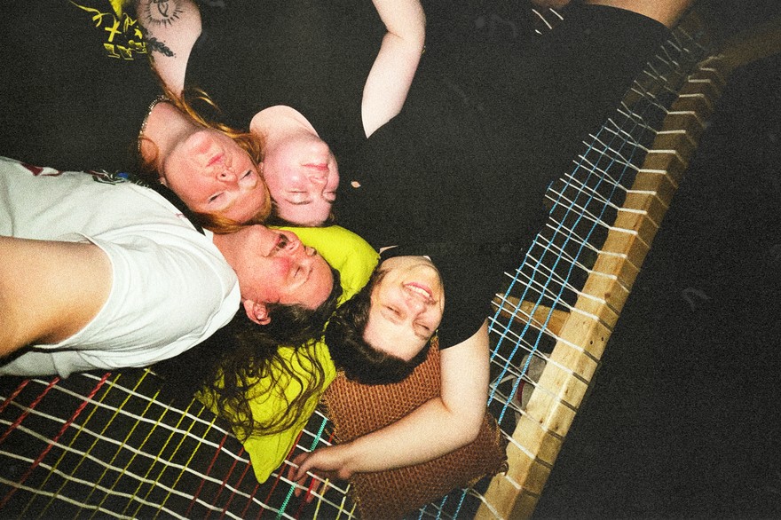 A grainy colour photo shows four members of the group Sick Puppy laying in a hammock looking up with the photo being taken from above.