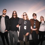 A slightly blurry photo shows five-piece band Sub / / Cell standing on a white bridge with each member wearing sunglasses. A blue and light purple sky is shown behind them. 