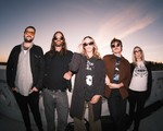 A slightly blurry photo shows five-piece band Sub / / Cell standing on a white bridge with each member wearing sunglasses. A blue and light purple sky is shown behind them. 