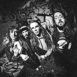 A black and white photo shows the group Tall Mary standing in front of a graffitti wall, each staring into the camera which has a warped vignette effect.